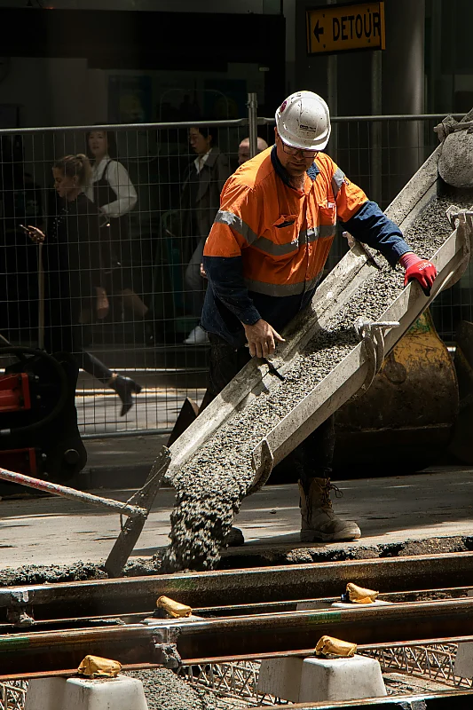 Construction worker in a hi-vis vest placing concrete from a chute on a work site