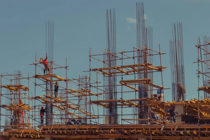 Construction crew working on scaffolding around steel rebar columns during a new build