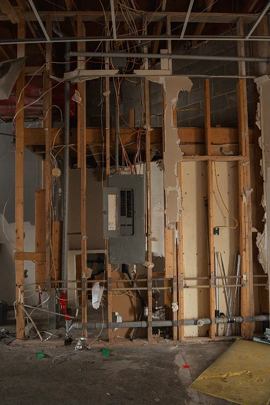 Home interior stripped back to bare framing mid-renovation, showing studs and an electrical panel
