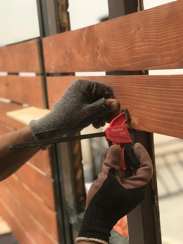 Gloved carpenter clamping cedar boards while building a slat feature wall during a renovation