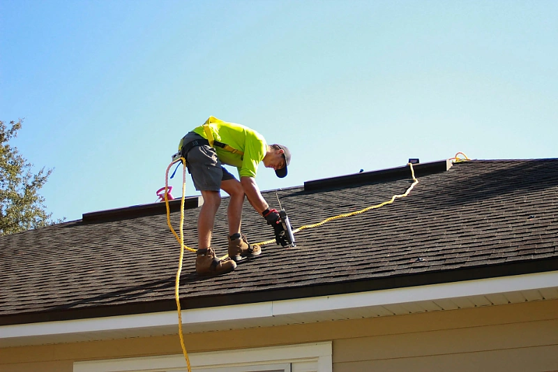 Double G Construction roofer in a safety harness installing asphalt shingles on a home roof in Kamloops, BC