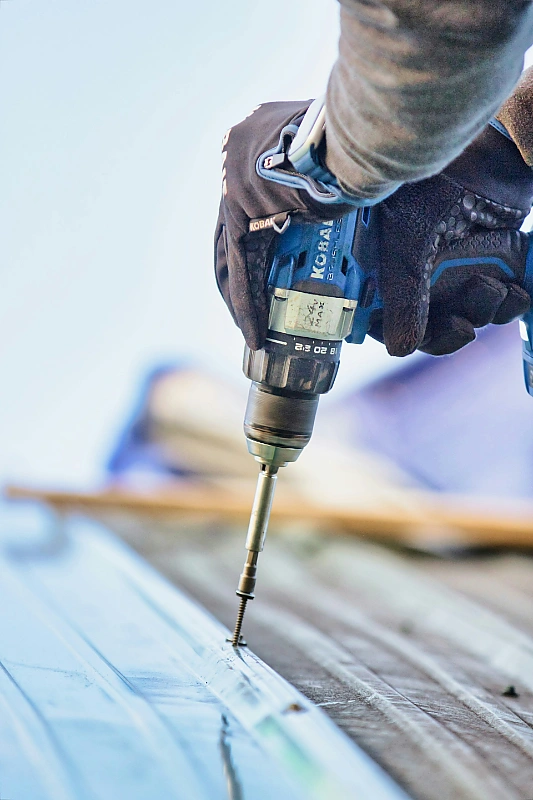 Close-up of a roofer fastening a metal roofing panel with a cordless drill